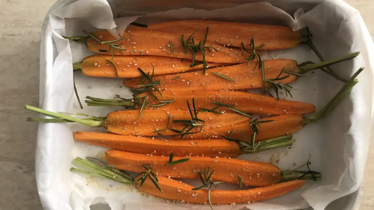 Carote al forno, tagliate a metà, condite con rosmarino e semi di sesamo, pronte per essere infornate.