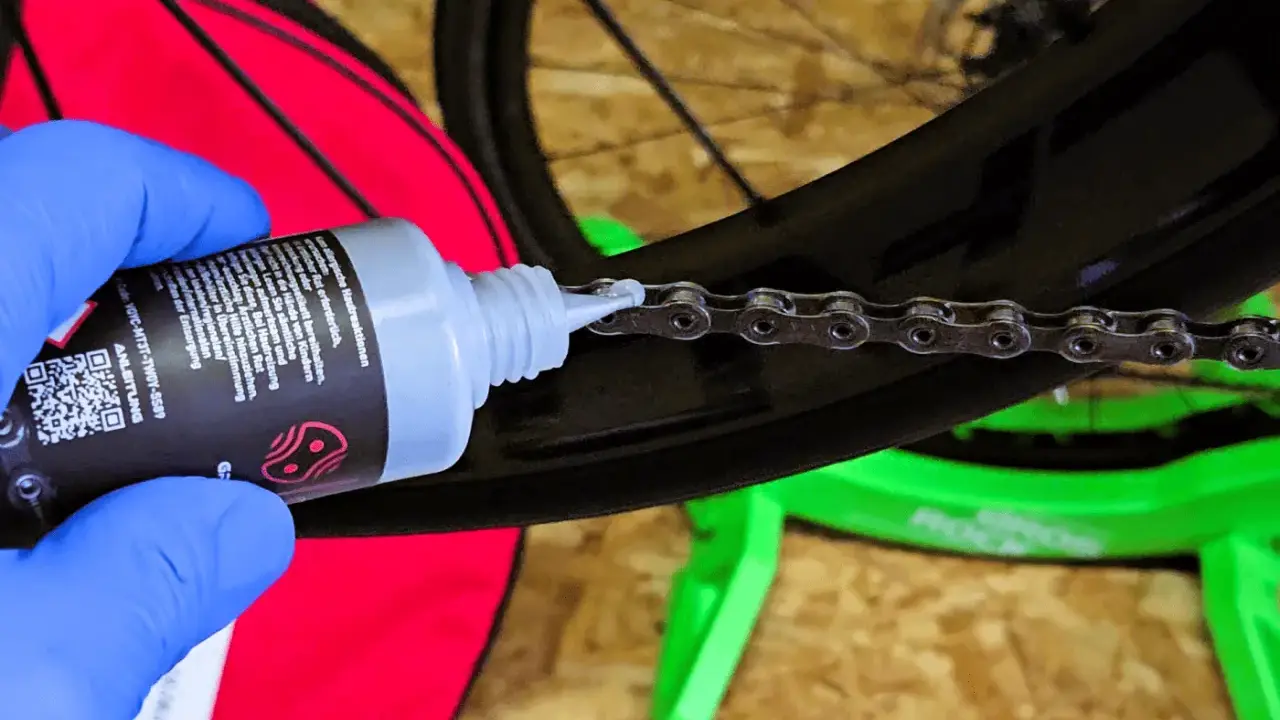 Blaue Handschuhe tragen, um die Fahrradkette wachsen zu lassen. Ein Tropfen Öl fällt auf die Kettenglieder.