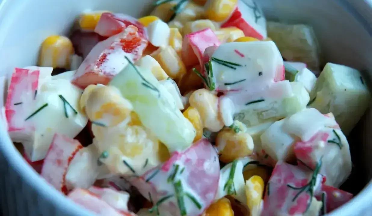 Pyszna sałatka z surimi, kukurydzy, ogórka i jajka, polana kremowym sosem z koperkiem.