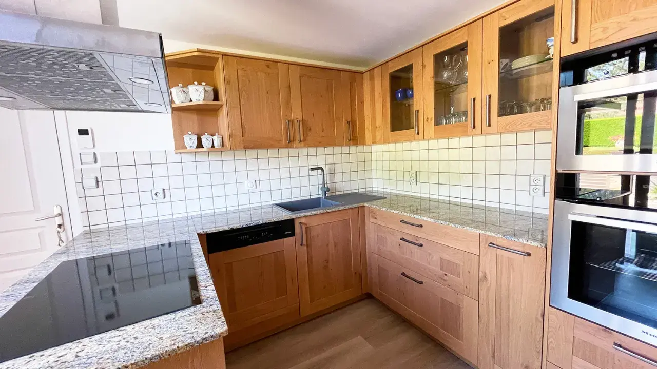 Cuisine en bois clair, avec des placards vitrés rappelant l'intérieur d'un voilier. Le plan de travail en granit et les appareils modernes complètent ce décor chaleureux.