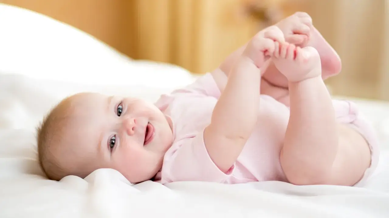 Ein lächelndes Baby von 8 Wochen liegt auf dem Rücken und spielt mit seinen Füßen.
