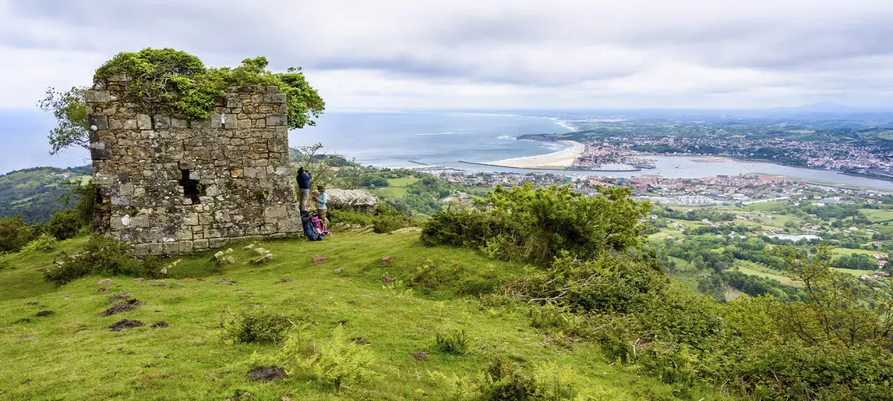 Zwei Wanderer genießen die Aussicht auf die Küstenstadt Irun, Spanien, von einer alten Ruine aus.