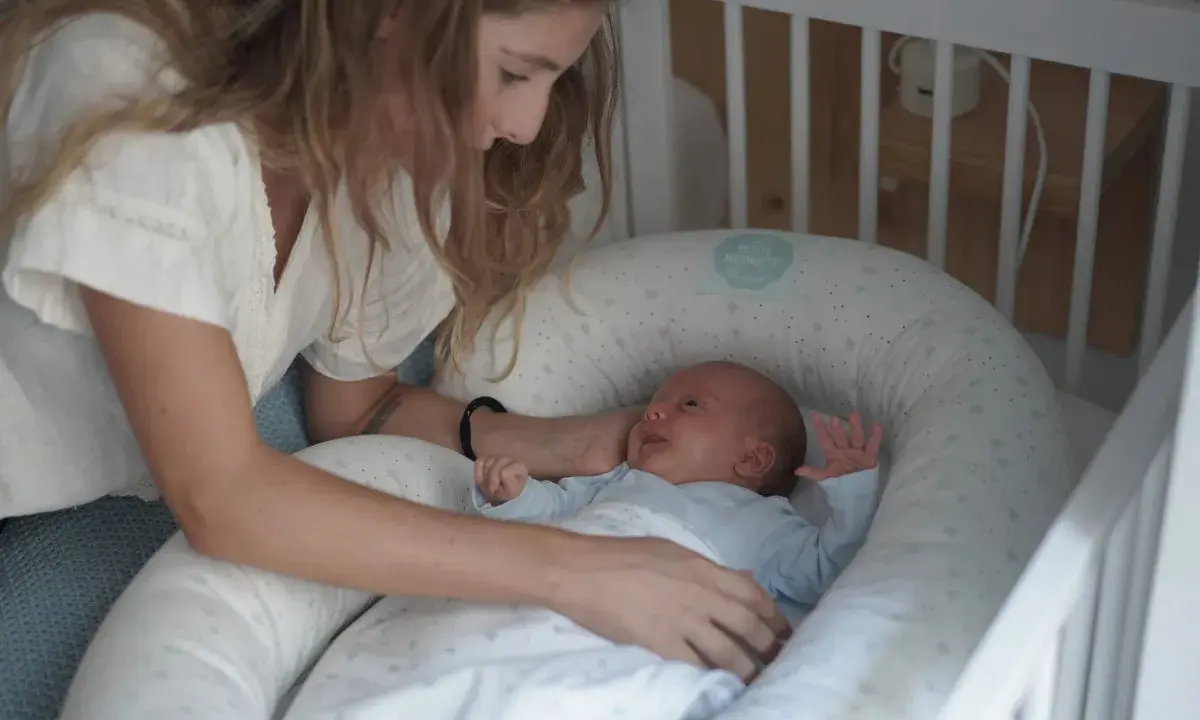 Madre observa a su bebé recién nacido, listo para sus siestas. El pequeño sonríe en su nido acogedor.
