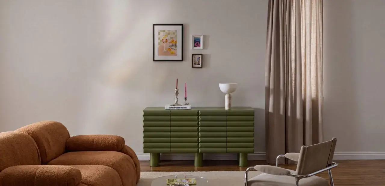 Un salotto moderno con divano color caramello, un mobile verde a coste e un gruppo di quadri appesi in modo originale.