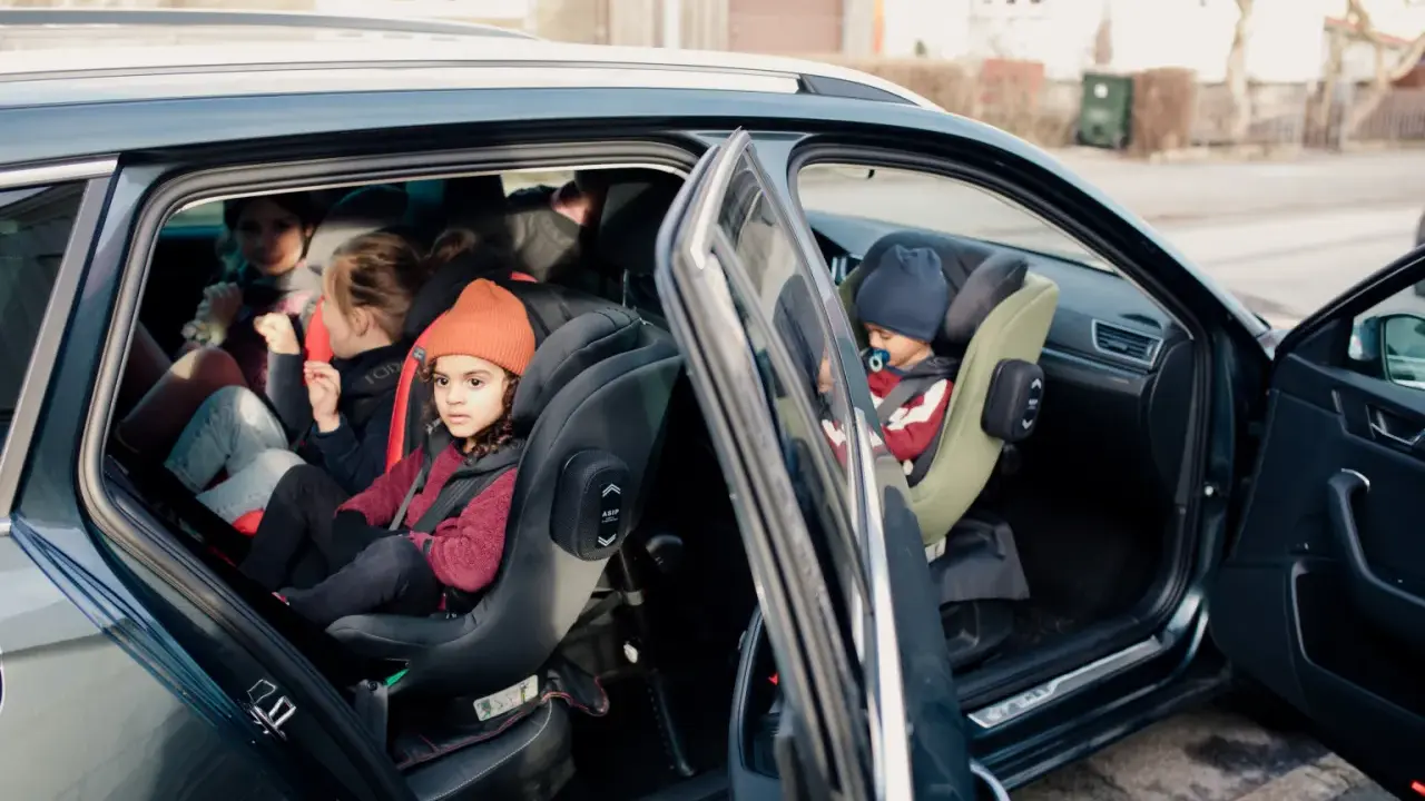 Niños en asientos de coche, uno con gorro naranja. Guía visual para como colocar silla grupo 2 3 sin isofix.