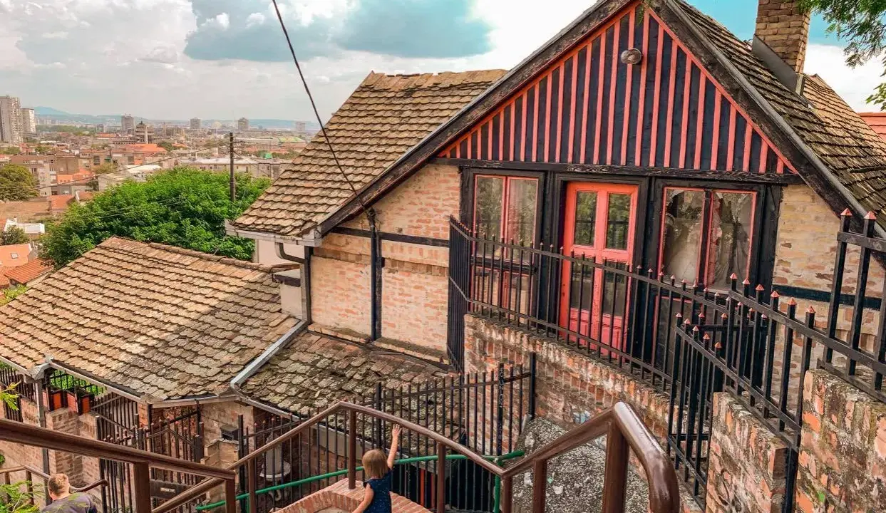 Schody prowadzące do urokliwego domu z różowymi drzwiami. Widok na panoramę miasta, idealne miejsce, by odkryć, co zobaczyć w Belgradzie.