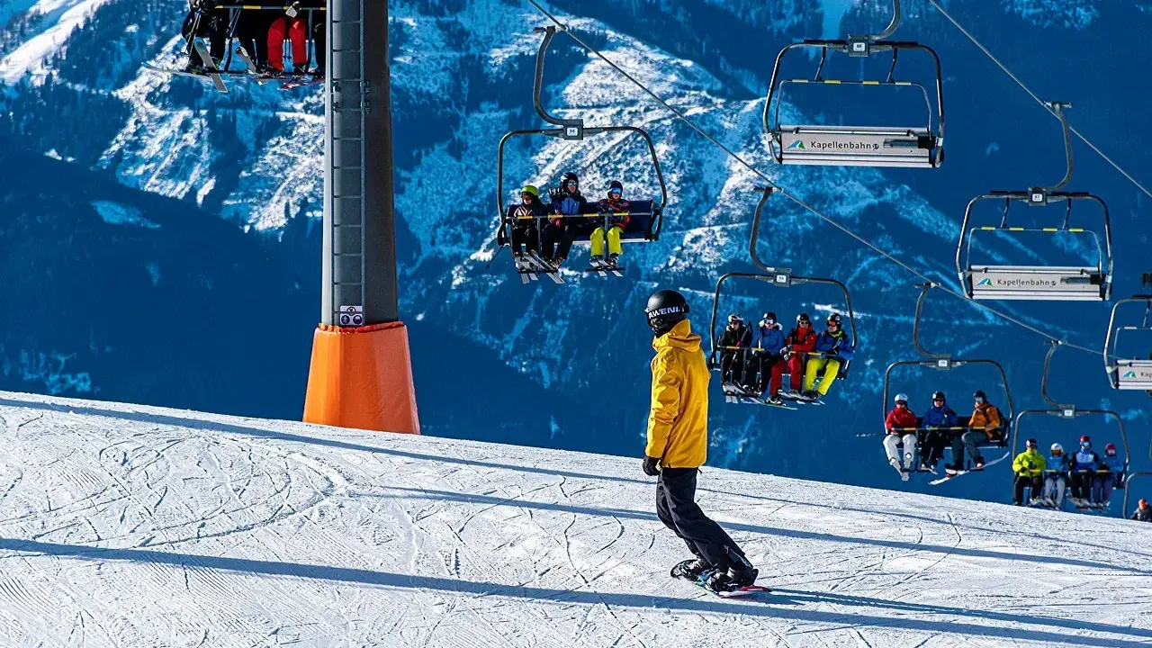 Snowboarder na stoku pod kolejką linową z narciarzami.