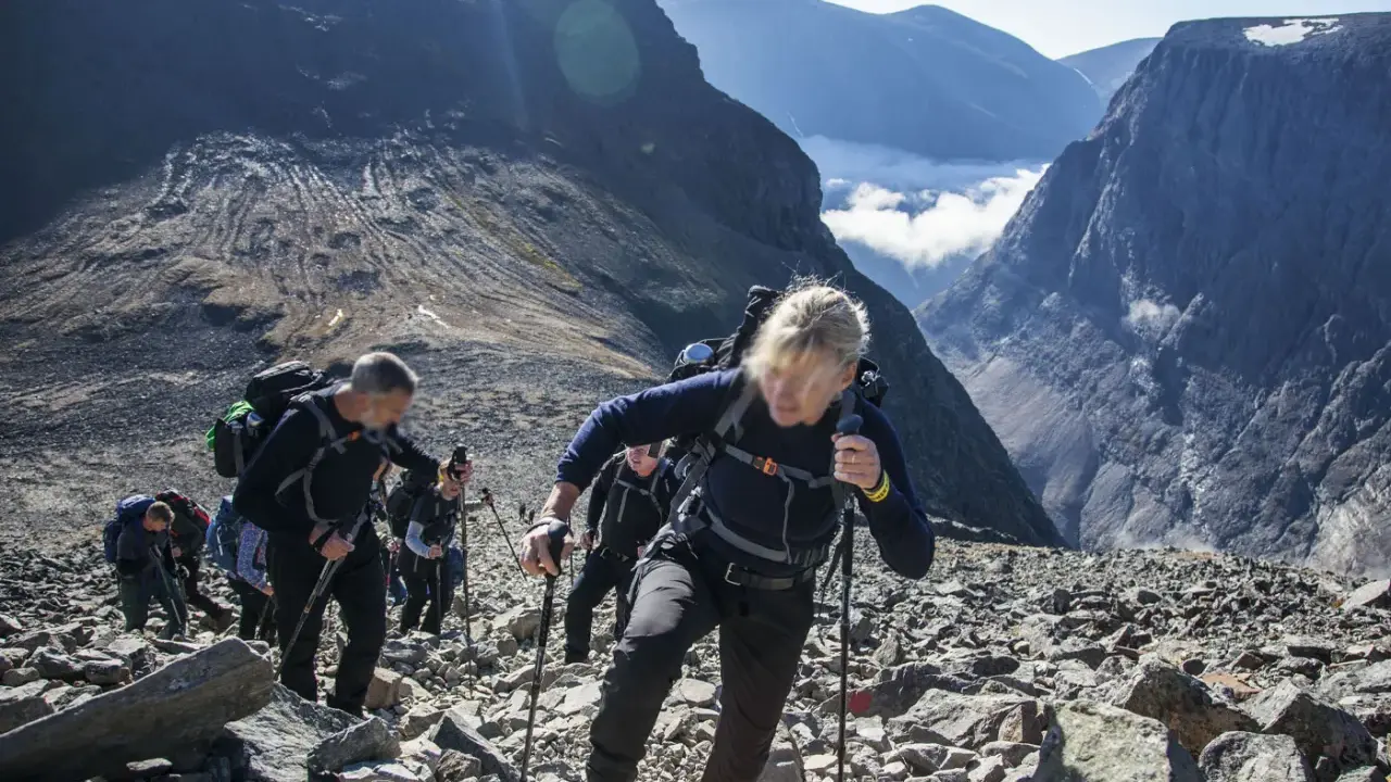 Vandring uppför stenigt landskap mot Sveriges högsta berg. Moln och bergstoppar i bakgrunden.