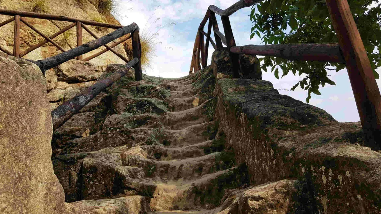 Antica scala in pietra scavata nella roccia, con ringhiera in legno, che conduce verso l'alto, evocando un'esplorazione in una grotta in Calabria.