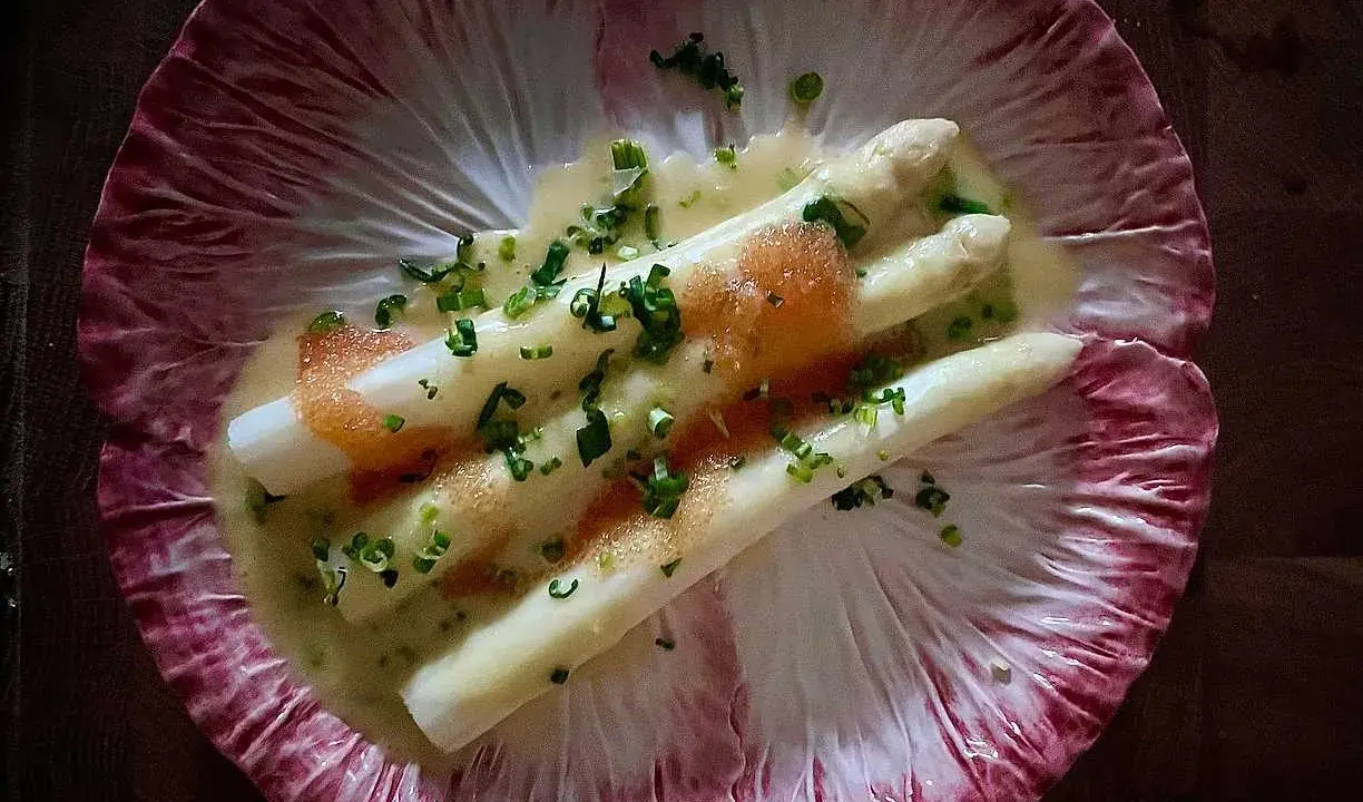 Vitt sparris med en krämig sås, toppad med kaviar och gräslök, serverad på ett rött endiveblad. En delikat ansa sparris.