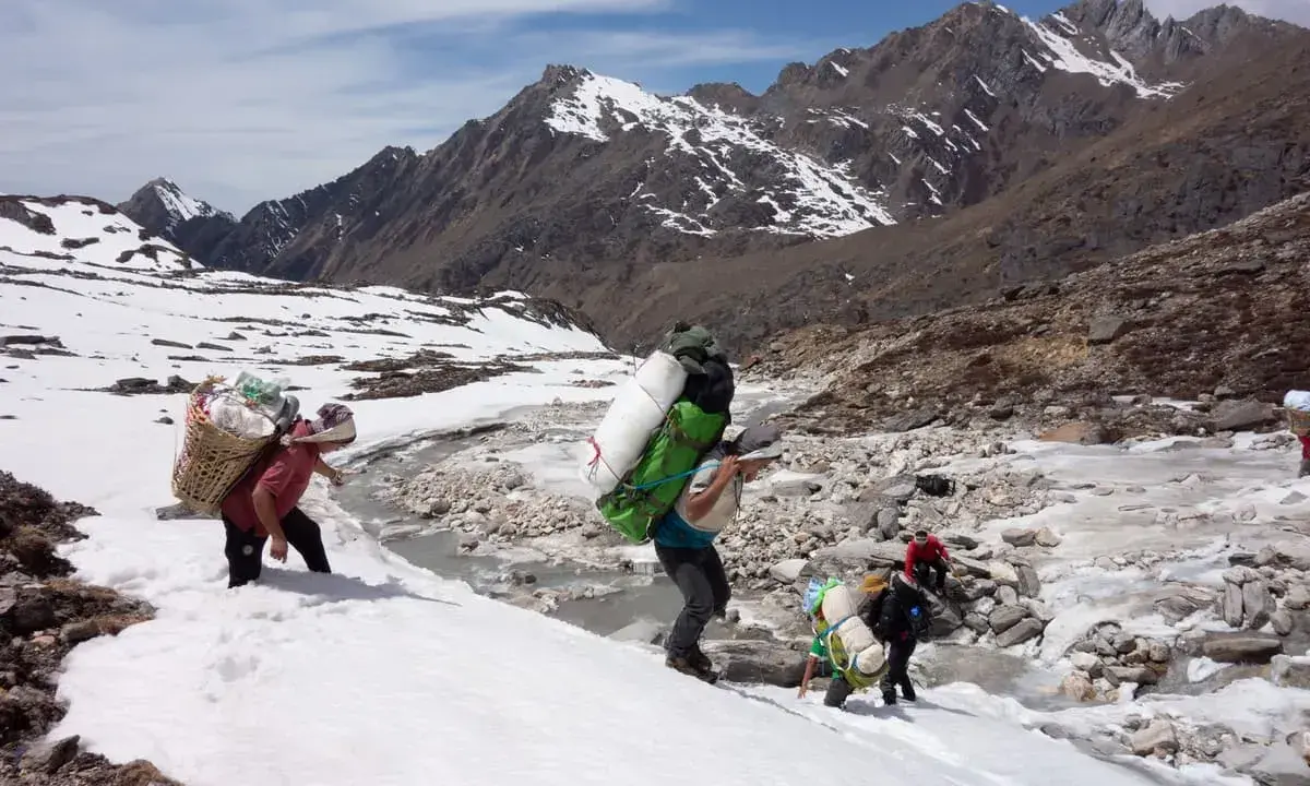 Ludzie niosący ciężkie ładunki w śniegu, zbliżając się do mount everest base camp. Góry w tle.