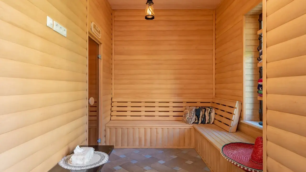 Interior de madera con bancos para relajarse, mostrando varios tipos de saunas. Un sombrero rojo y cojines decoran el espacio.