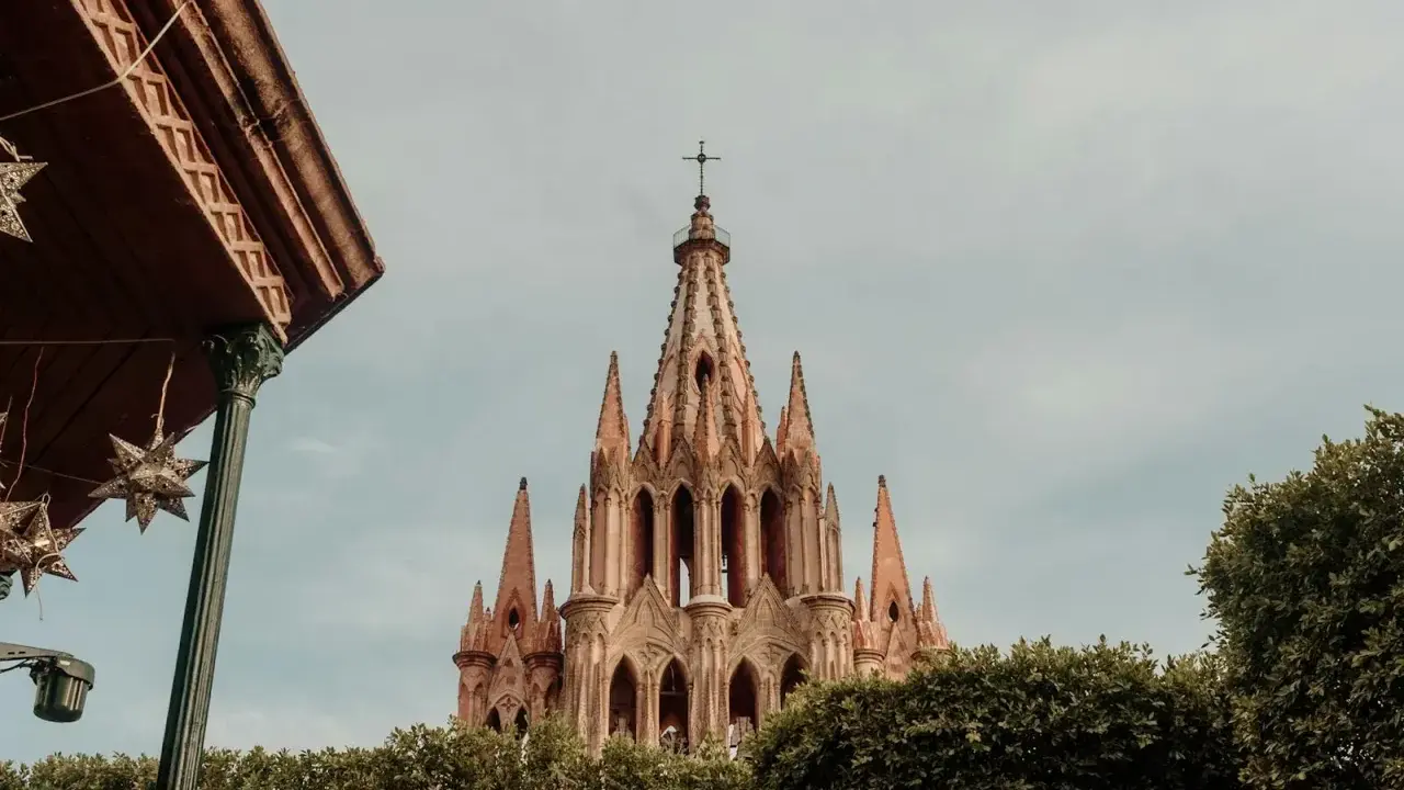 Imponująca iglica kościoła w San Miguel, otoczona zielenią, z ozdobnymi gwiazdami zwisającymi z zadaszenia.