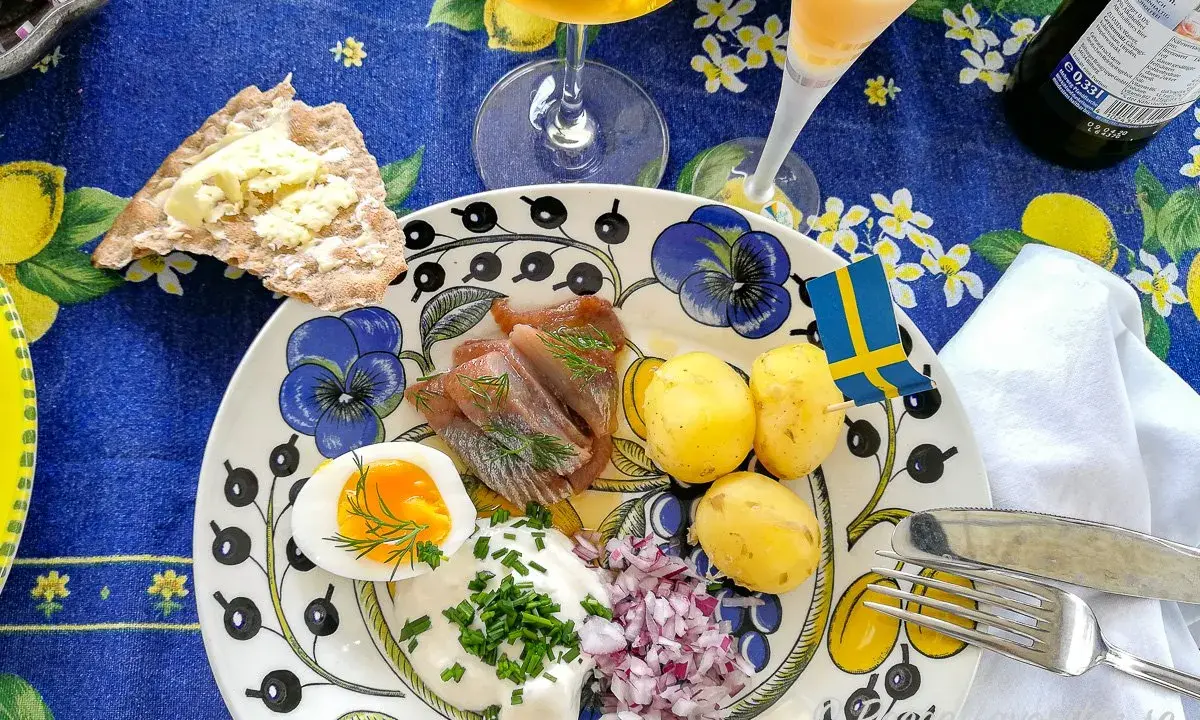 En härlig sillunch midsommar med färskpotatis, ägg, gräddfil och rödlök. En svensk flagga vajar glatt.