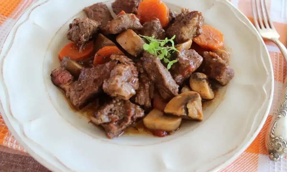 Bœuf bourguignon: duszona wołowina z marchewką i pieczarkami, podana na talerzu.
