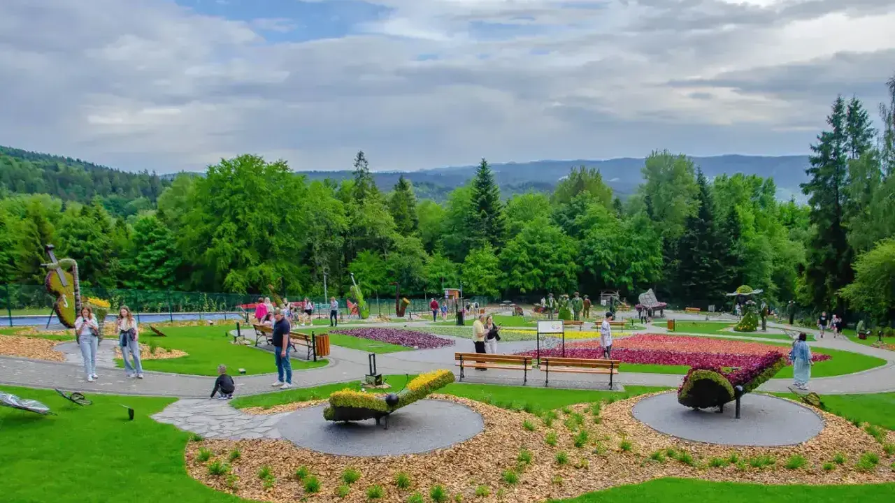 Kolorowy park z rzeźbami z kwiatów i zieleni. Widać ludzi spacerujących alejkami. Sprawdź góra parkowa cennik, by zaplanować wizytę.