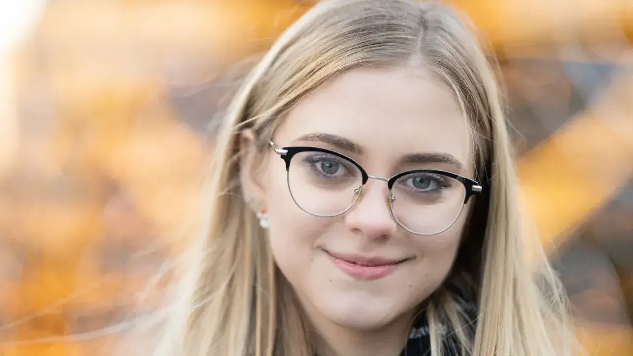 Uśmiechnięta blondynka w okularach, z rozmyciem tła. Idealna ogniskowa do portretu, podkreślająca oczy.