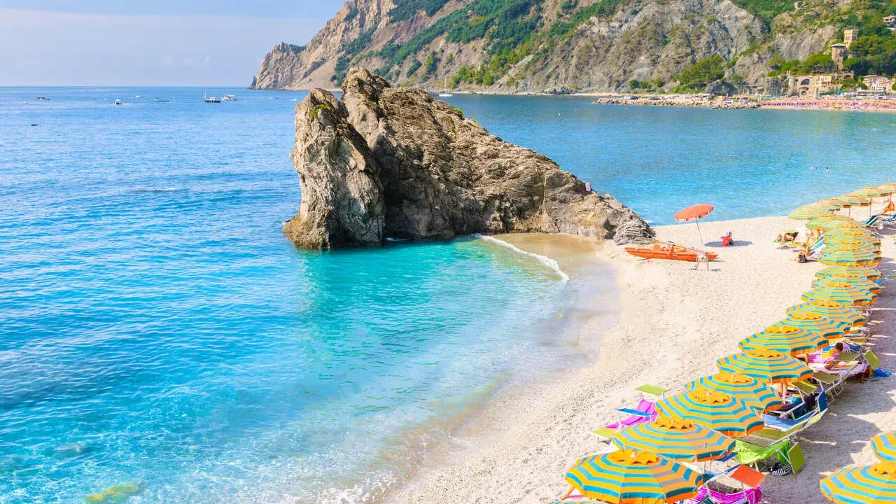 Ein malerischer italien strand mit türkisfarbenem Wasser, einem Felsen im Meer und vielen bunten Sonnenschirmen.