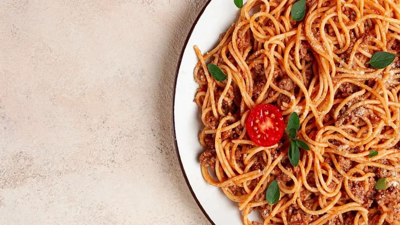 Pyszne spaghetti z mięsem mielonym, udekorowane pomidorkiem i listkami bazylii. Idealne na szybki obiad.