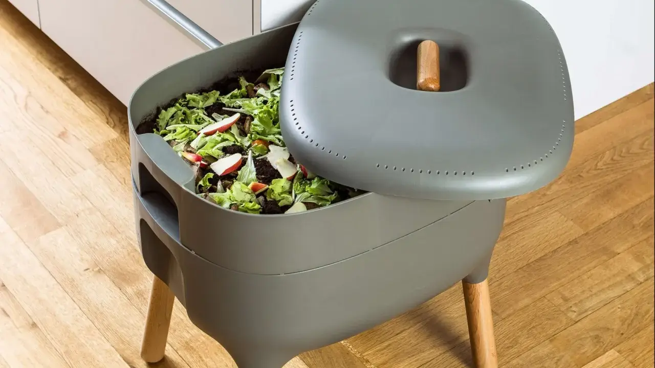 Compostador gris con restos de comida y hojas. Aprende como hacer compost para un jardín sostenible.