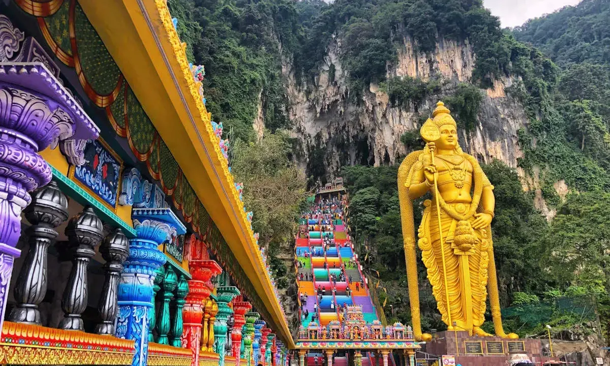Kolorowe schody Batu Caves w Malezji, prowadzące do jaskini, obok złotej statuy boga Murugana. Warto zobaczyć!