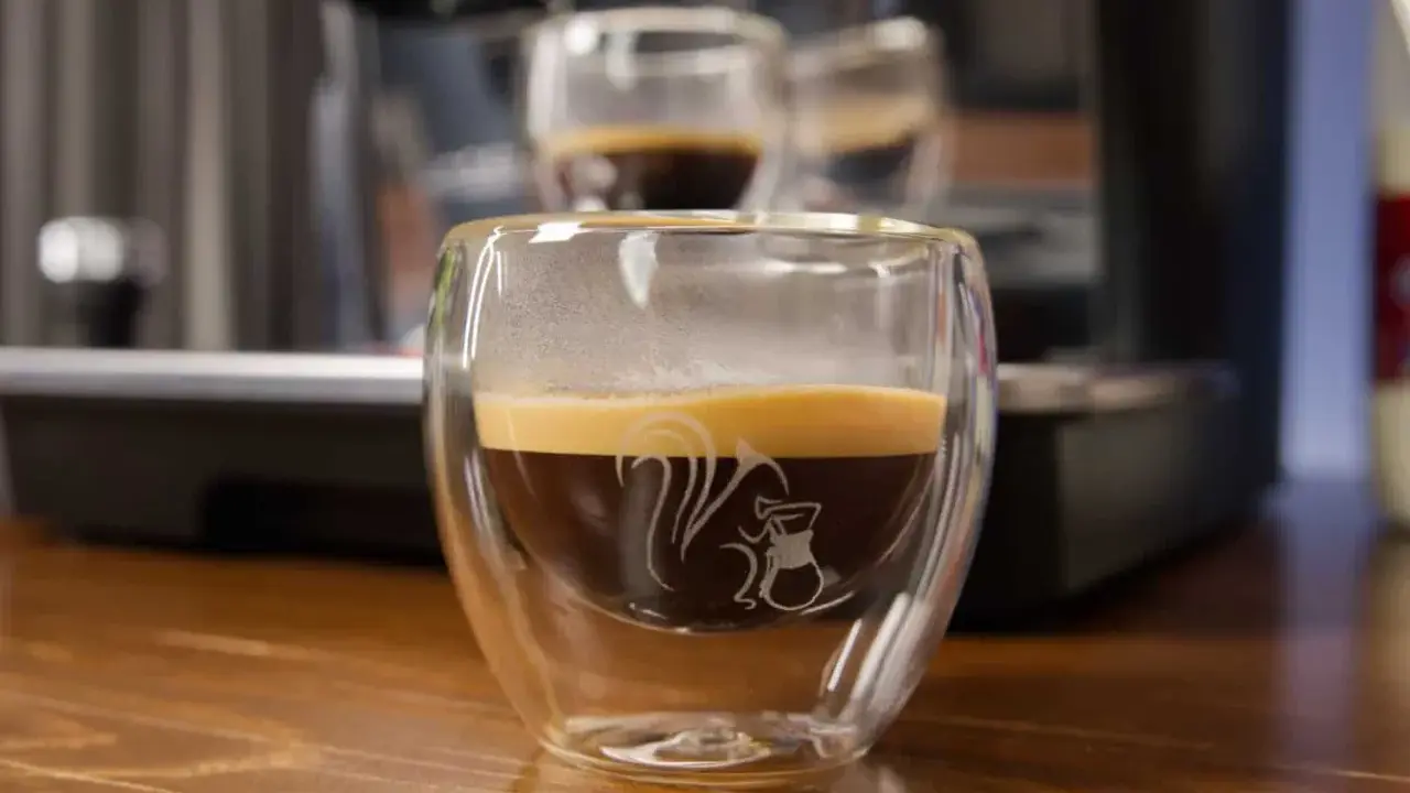 Ein dampfender doppio macchiato in einem doppelwandigen Glas mit einem Eichhörnchen-Motiv.