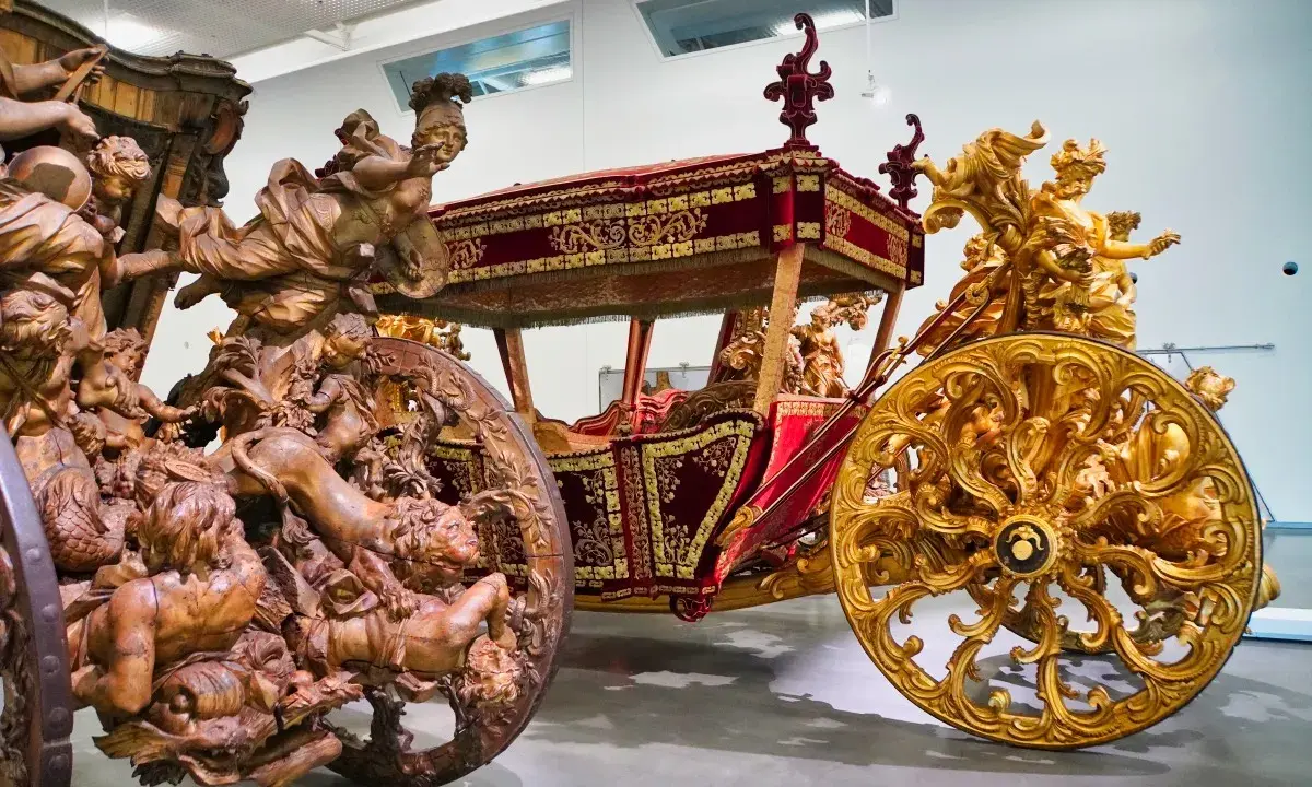 Prunkvolle Kutschen im Kutschenmuseum Lissabon: Eine aus Holz geschnitzte, die andere golden verziert, beide mit aufwendigen Figuren.