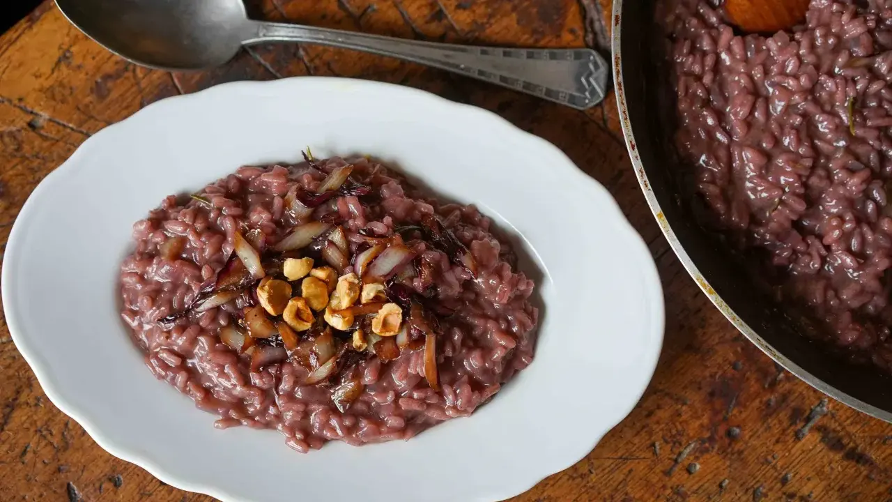 Risotto rosso con cipolla caramellata e nocciole, un classico tra i piatti tipici di Verona, servito su un piatto bianco con un cucchiaio d'argento.