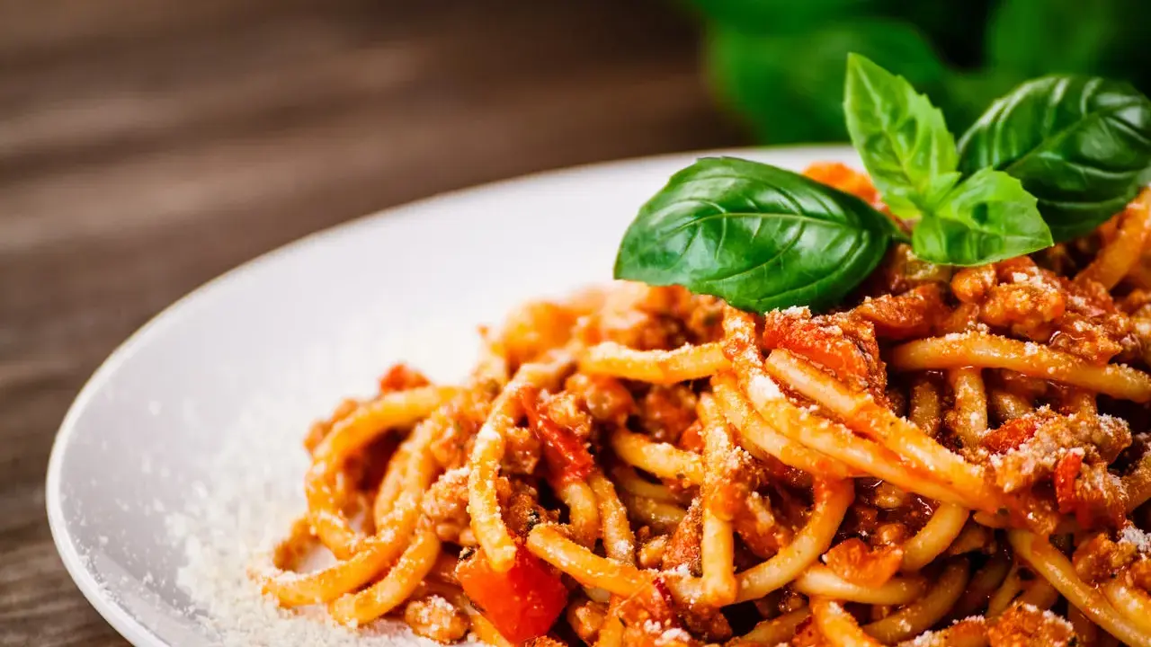 Pyszne spaghetti z bogatym sosem mięsnym, posypane parmezanem i udekorowane świeżą bazylią. Idealny sos do spaghetti na obiad.