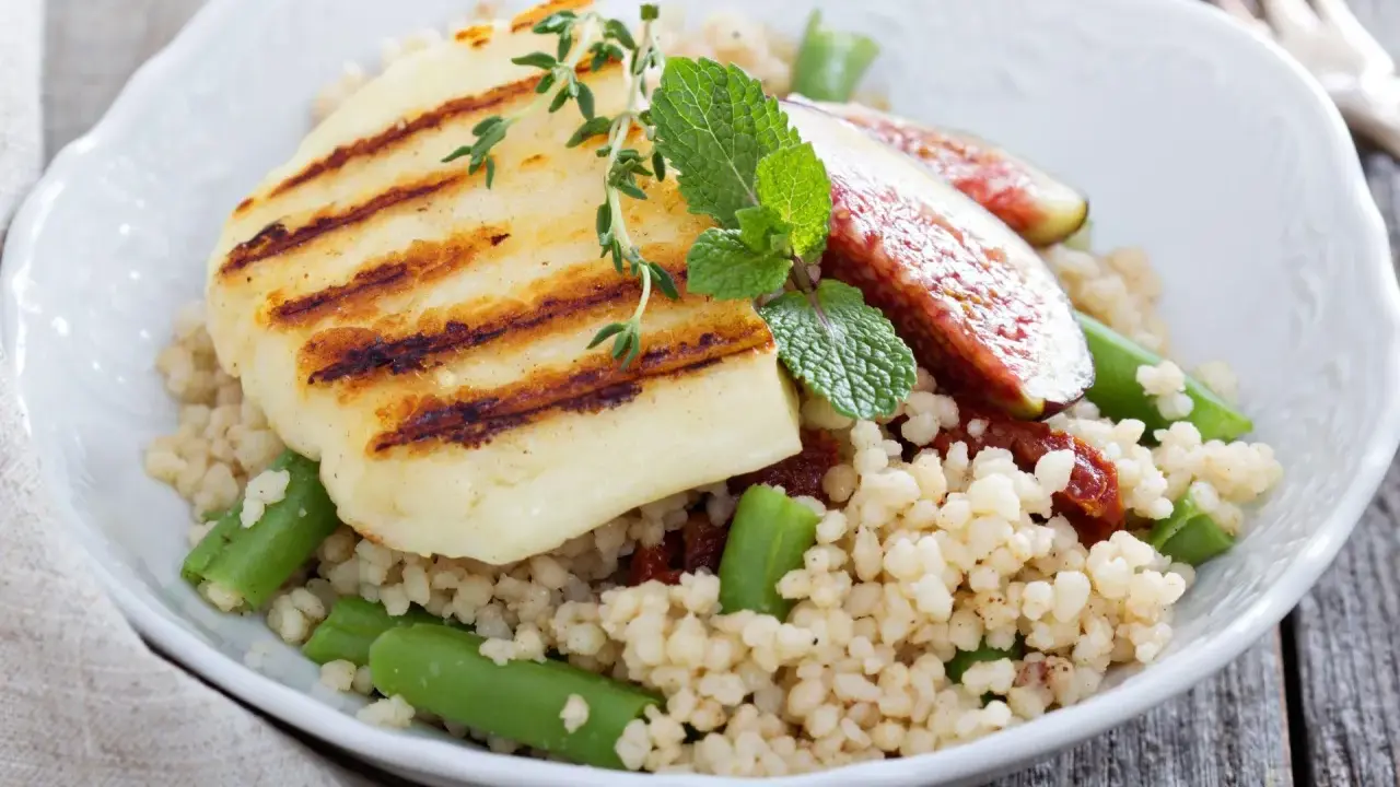 Kuskus z grillowanym serem halloumi, fasolką szparagową i figami, ozdobiony miętą.