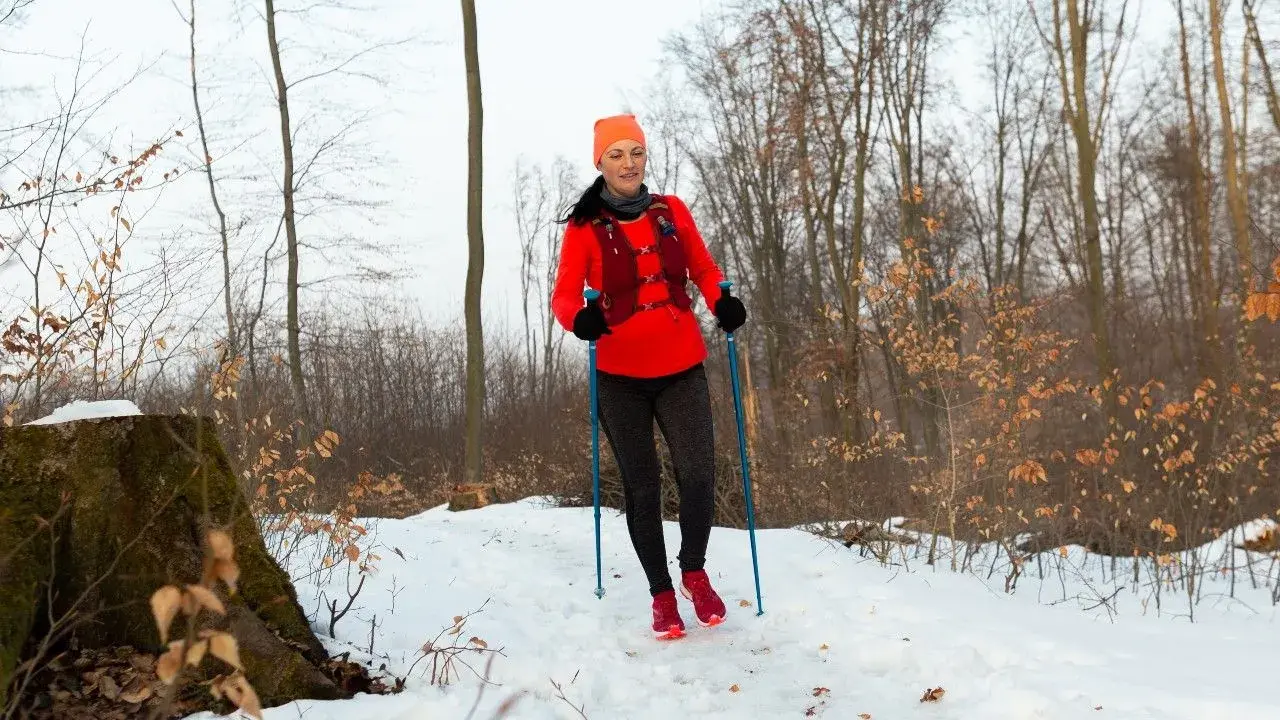 Kobieta w lesie zimą, ćwicząca nordic walking. Końcówki do kijków nordic walking zapewniają stabilność na śniegu.