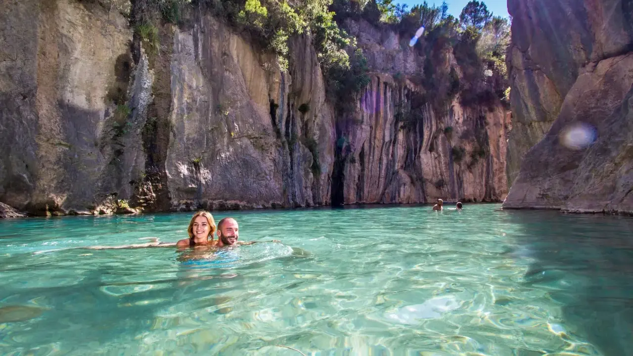 Pareja nadando en aguas cristalinas rodeados de acantilados. ¡Una gran idea de qué hacer en Castellón con niños!