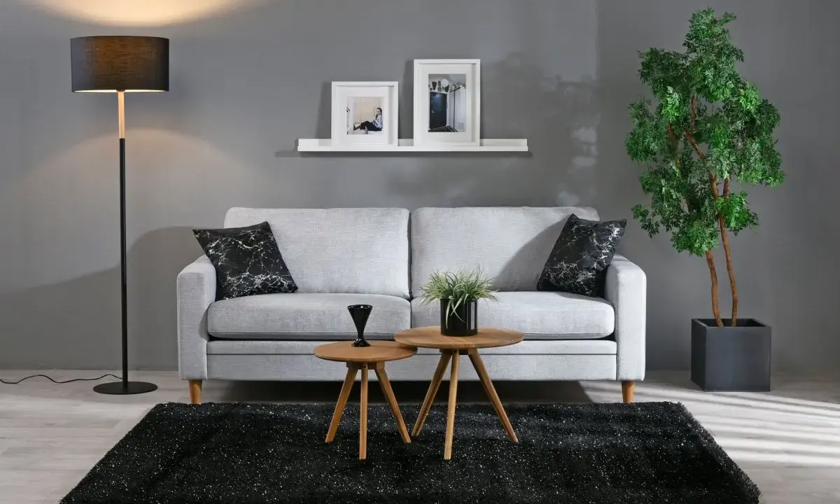 En stilren inredning grått med en ljusgrå soffa, svart matta och en golvlampa. Två runda bord framför soffan.