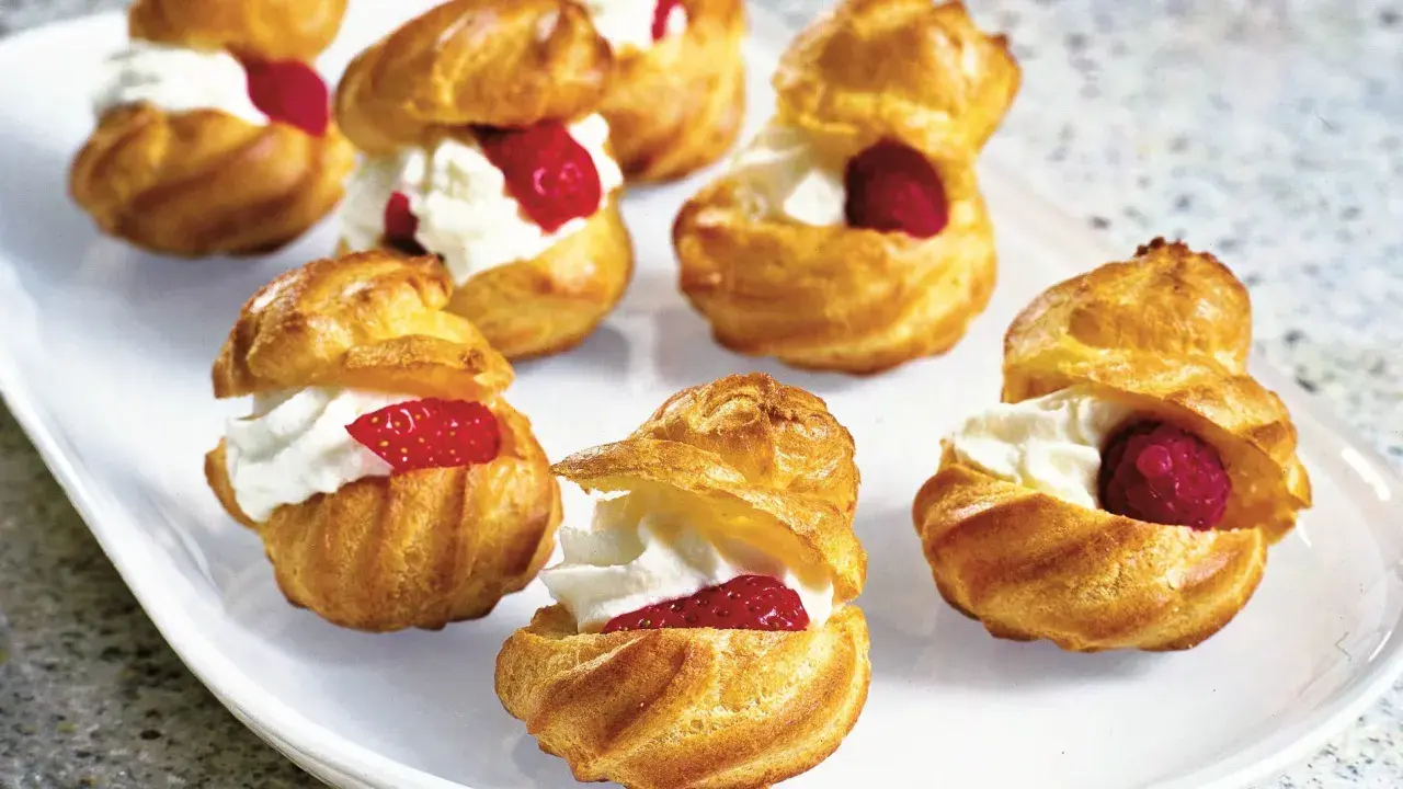 Små petit choux fyllda med vispgrädde och toppade med hallon eller jordgubbar. En härlig dessert!