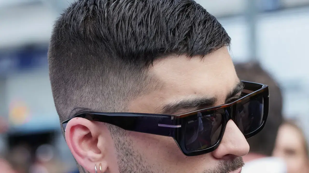 Mann mit stylischem Crew Cut und Sonnenbrille, der nachdenklich in die Ferne blickt.