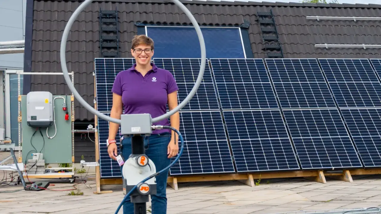Kvinna med glasögon står framför solpaneler. Ett solceller montagesystem är synligt på taket.