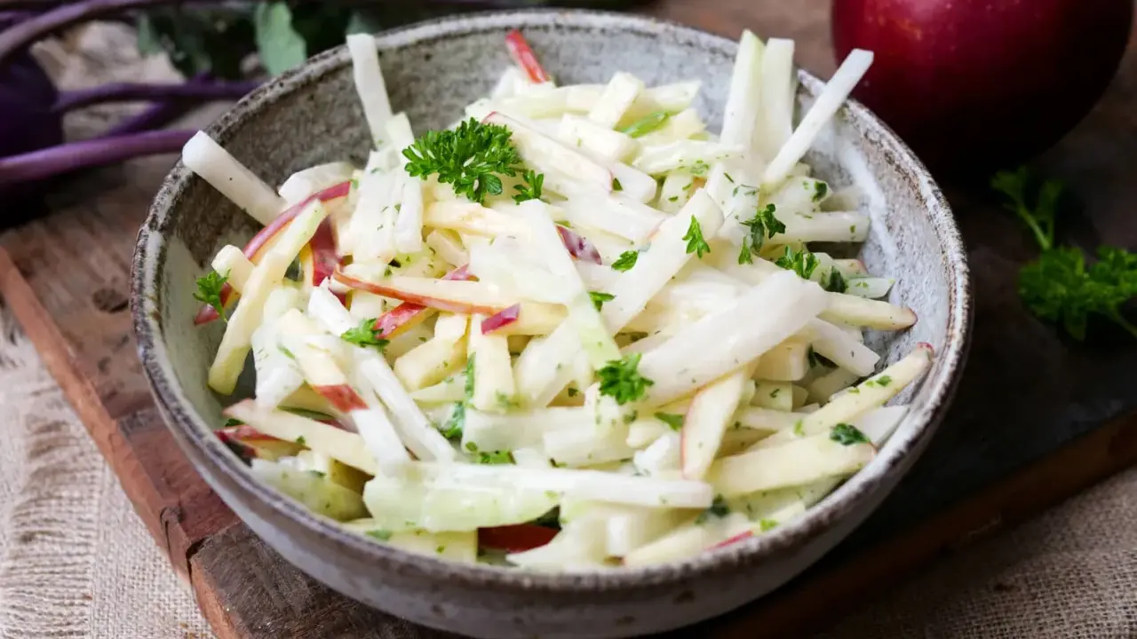 Kohlrabi Salat mit Apfelstücken und frischer Petersilie, garniert mit einem roten Apfel im Hintergrund.
