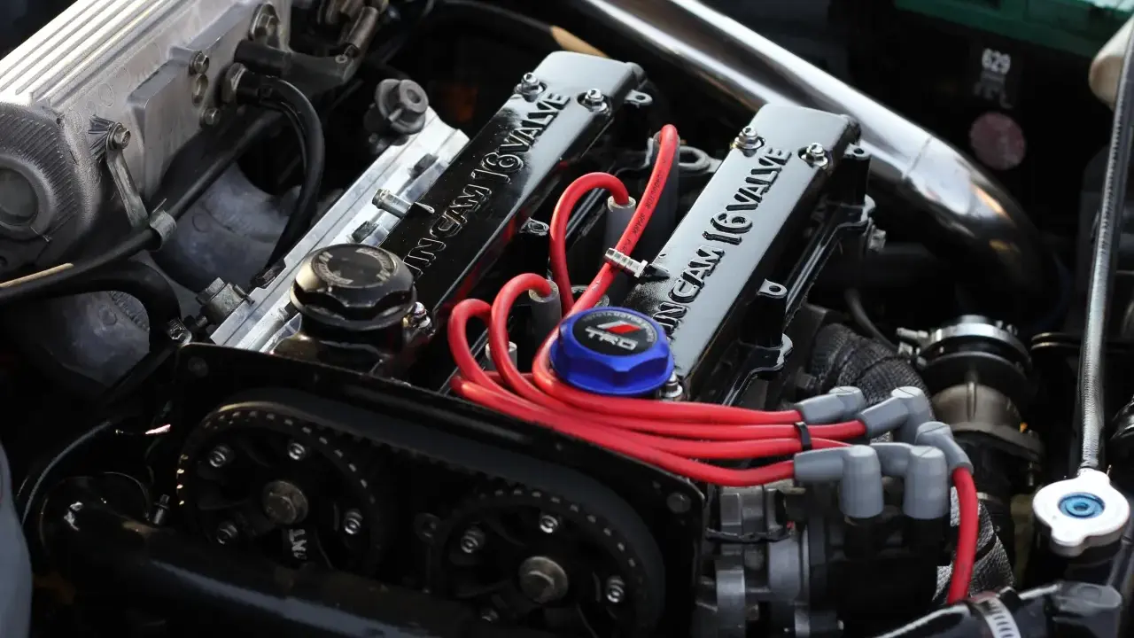 Motor de coche con tapa de válvulas "16 VALVE", cables rojos y correa de distribución.