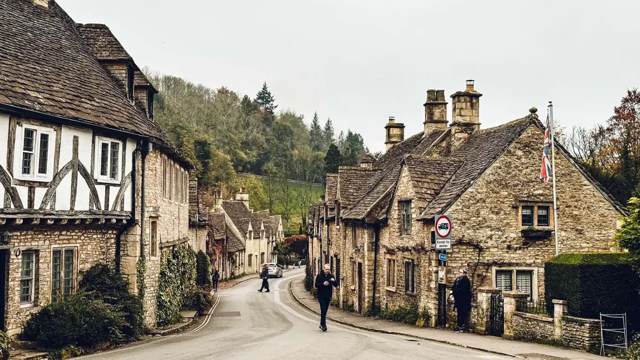 Kamienna uliczka w Cotswolds z tradycyjnymi domami i ludźmi spacerującymi po drodze.