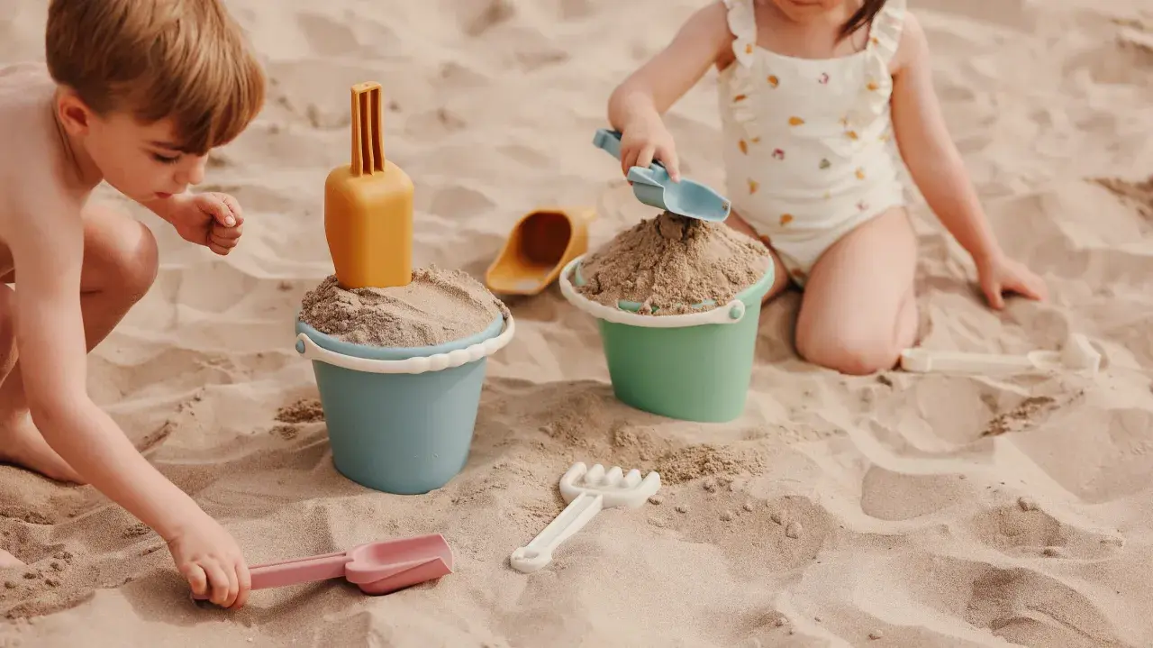 Niños disfrutando de juegos en la playa con cubos y palas de arena.