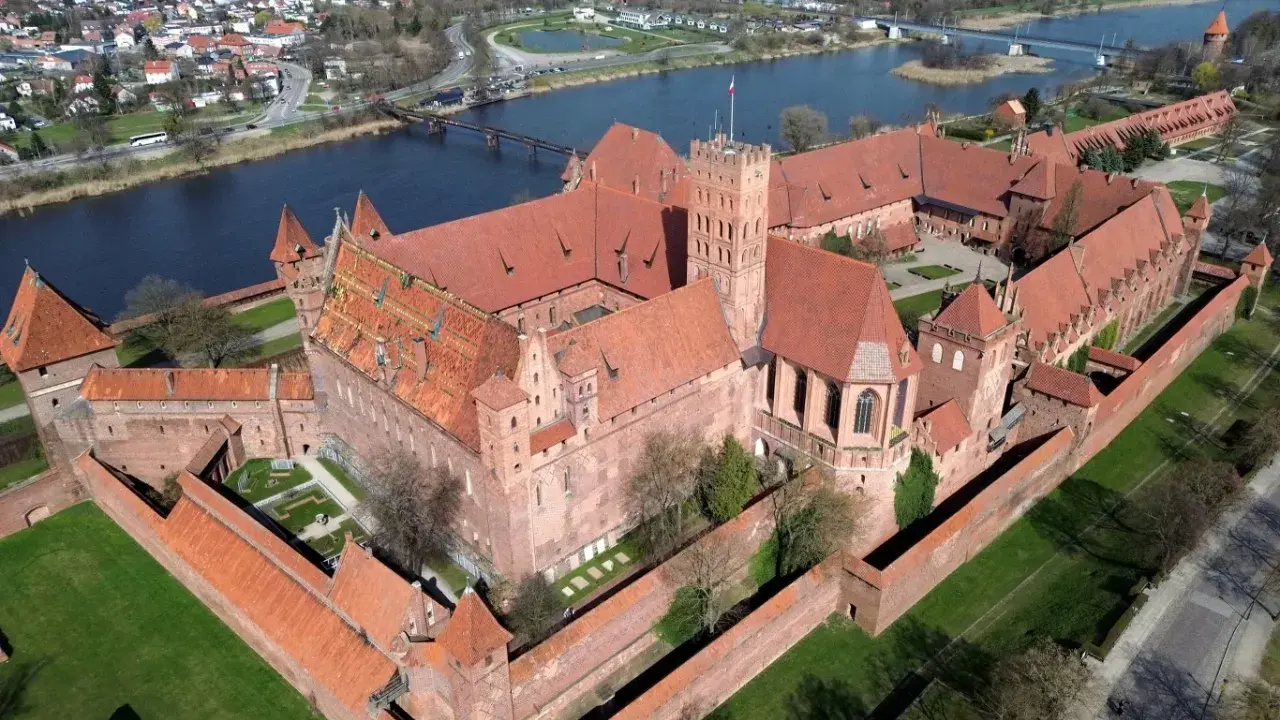 Malbork, największy zamek w Europie, rozciąga się wzdłuż rzeki, otoczony murami obronnymi i zielonymi dziedzińcami.