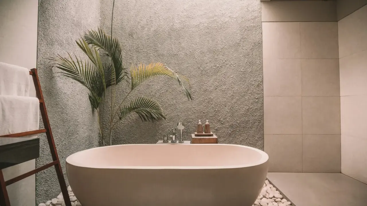 Elegante bañera exenta, rodeada de piedras blancas y una planta tropical. Muestra varios tipos de bañeras para un baño de lujo.