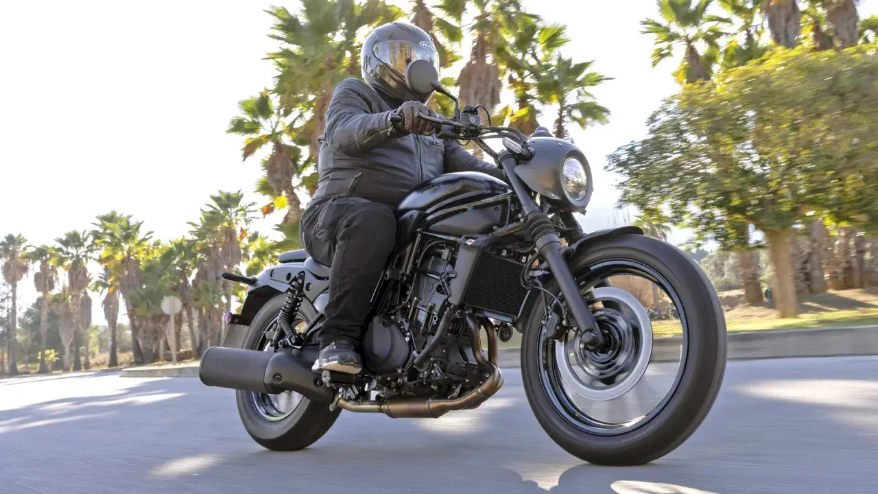 Mężczyzna w kasku jedzie czarnym motocyklem Kawasaki EN 500. Wady i zalety tego modelu są dyskutowane podczas jazdy wśród palm.