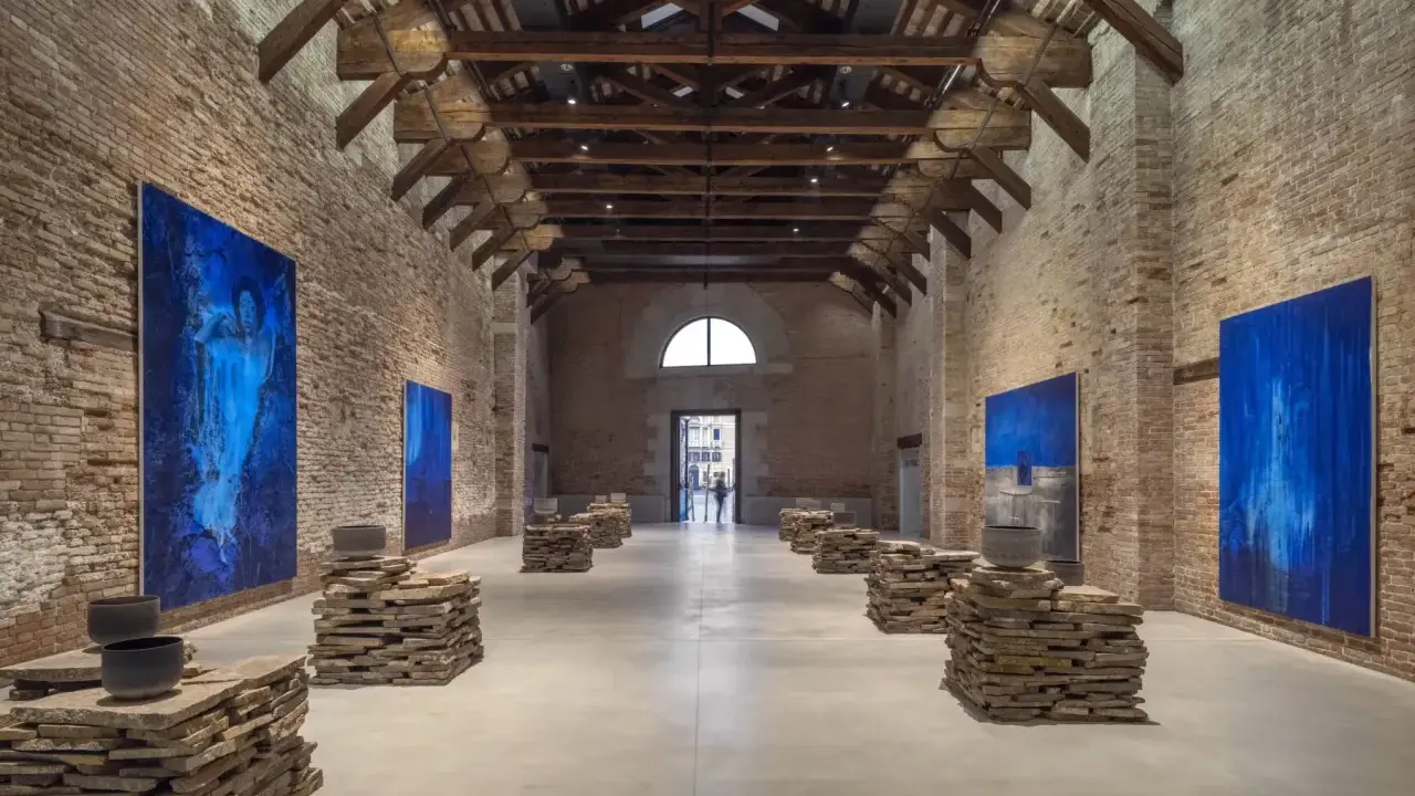 Vaste salle d'exposition à Venise, avec des œuvres d'art bleues et des sculptures en pierre. L'architecture industrielle de Pinault Venise est mise en valeur.