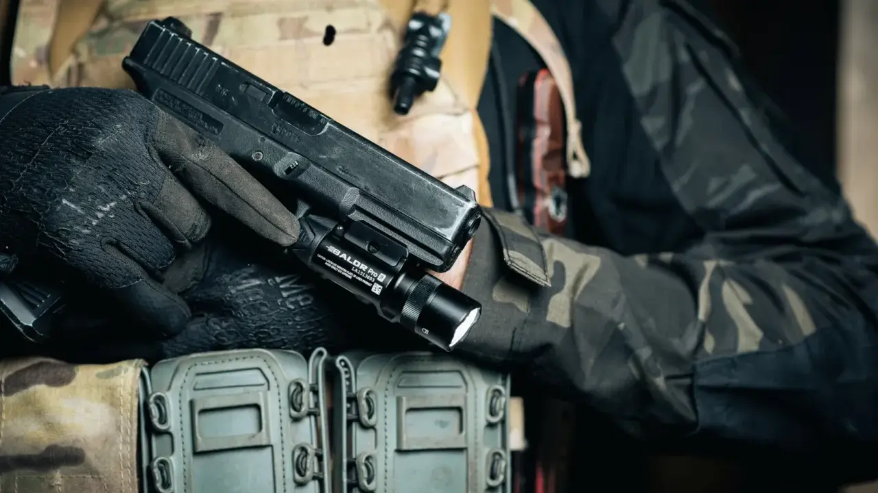 Dłoń w rękawiczce trzyma pistolet z zamontowanym na szynie taktycznym laserem do broni.