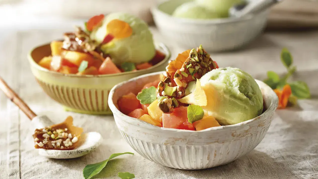 Deliciosos postres saludables: helado verde cremoso con trozos de melón, papaya y un toque crujiente de pistachos.