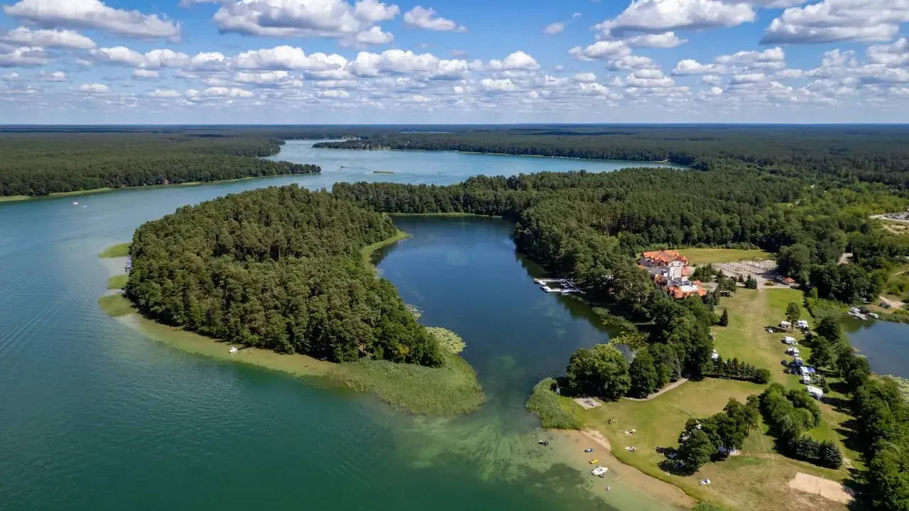 Malownicze jezioro Urszulewskie otoczone lasem, z hotelem i polem namiotowym na brzegu.