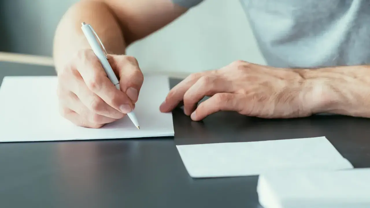 Mężczyzna pisze ręcznie list motywacyjny, przygotowując się do ważnego spotkania.