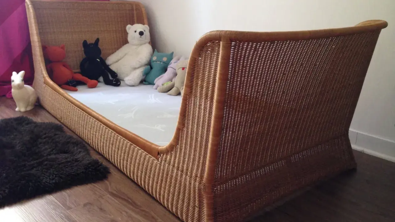 Lit en rotin tressé, style Louis Sognot, avec des peluches attendant patiemment dans un lit douillet.