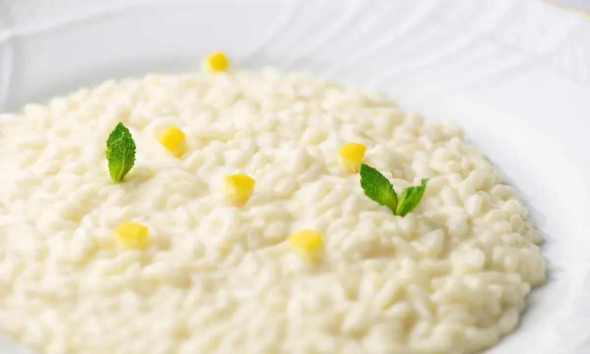 Un cremoso risotto al limone, guarnito con cubetti di limone e foglie di menta fresca, pronto per essere gustato.